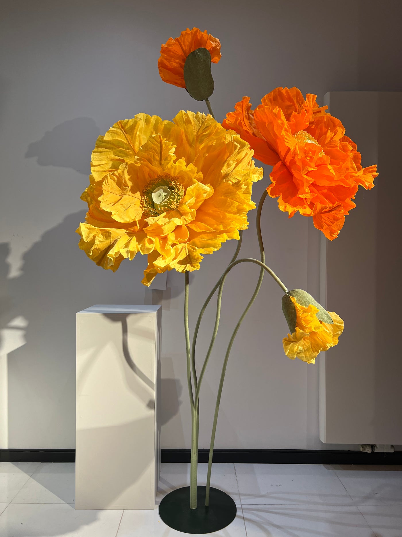 Trade Show Elegance: Giant Orange and Yellow Paper Flowers on Metal Stands