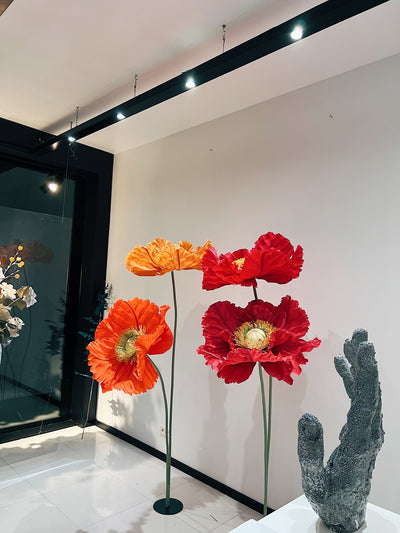 A group of four large, freestanding paper poppies in various shades of red, orange, and yellow, with detailed petals and light green centers.